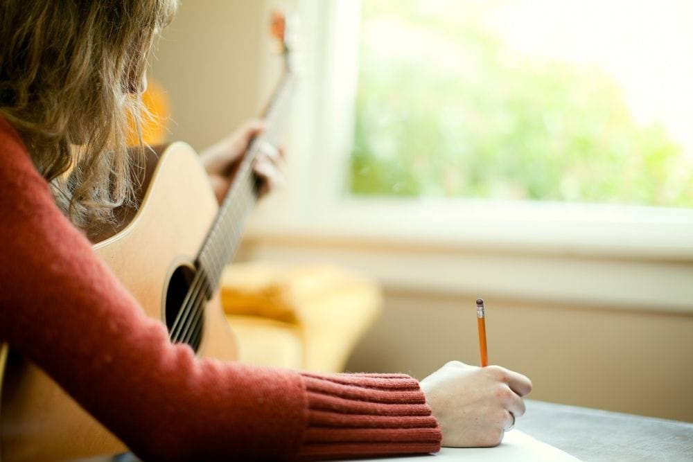 Woman with guitar writing down a bio