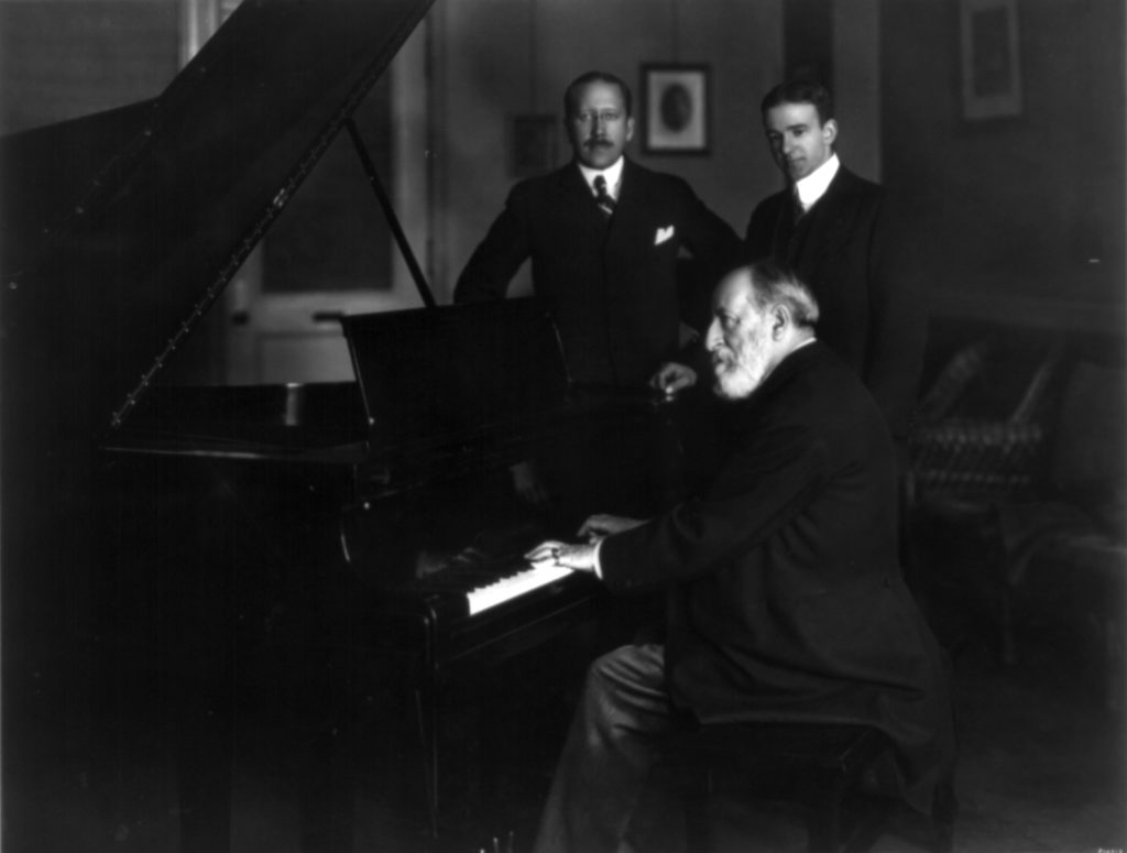 Photograph of Camille Saint Saëns playing piano while others watch
