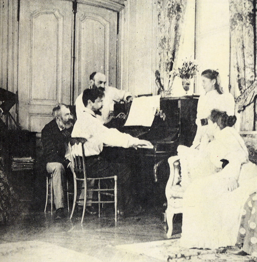 photograph of Claude Debussy playing piano while others watch on