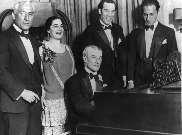 Photograph of Maurice Ravel playing piano with others posed behind him