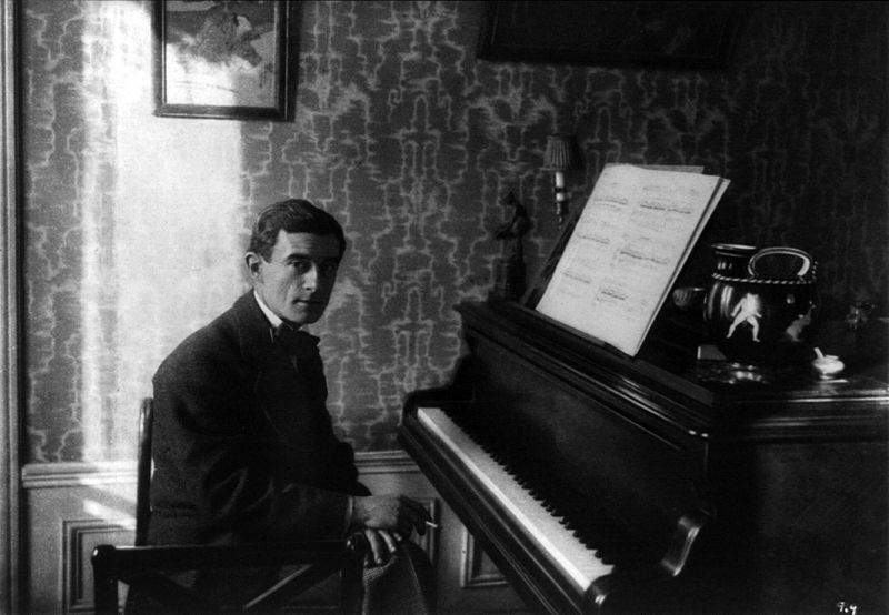Photograph of Maurice Ravel sitting next to a piano
