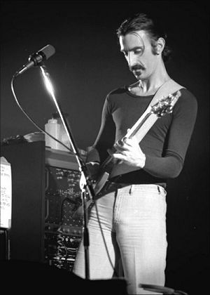 Musician Frank Zappa on stage playing guitar
