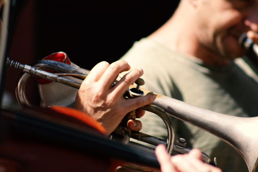 Close up on a man’s fingers on trumpet with another man playing trumpet in the background