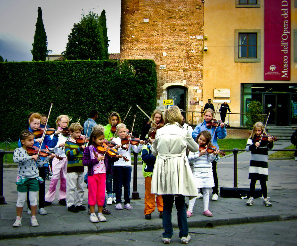 Children playing violins with a music teacher playing violin outside
