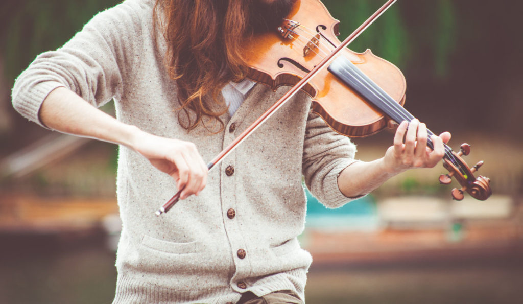 Woman in sweater playing violin outside
