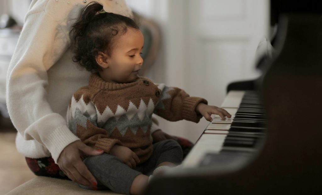 Young girl sitting in her mom's lap playing piano