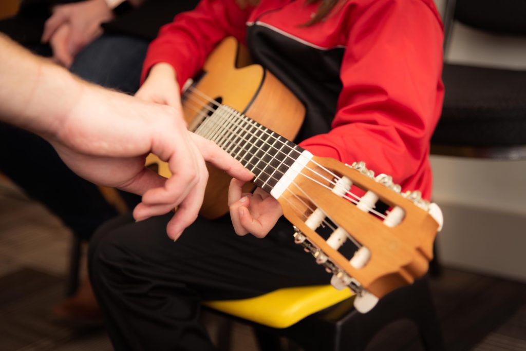 Child holding a guitar while the teacher points to where to put their hands