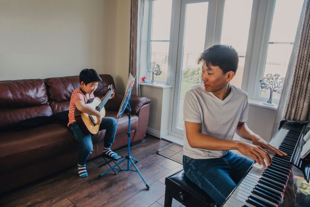 Young boy playing guitar with young man playing piano