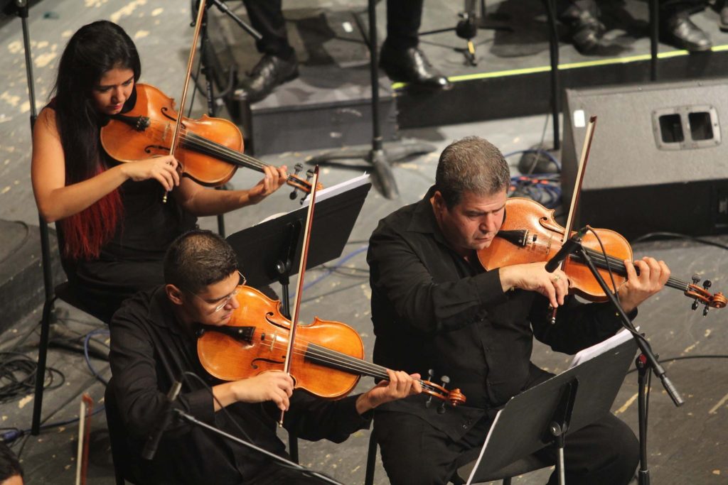 Three musicians playing the violin in an orchestra
