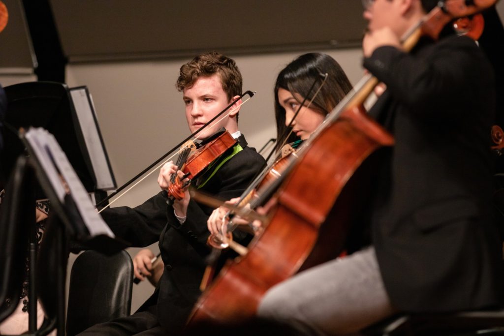 Three students playing the violin and cello in an orchestra 
