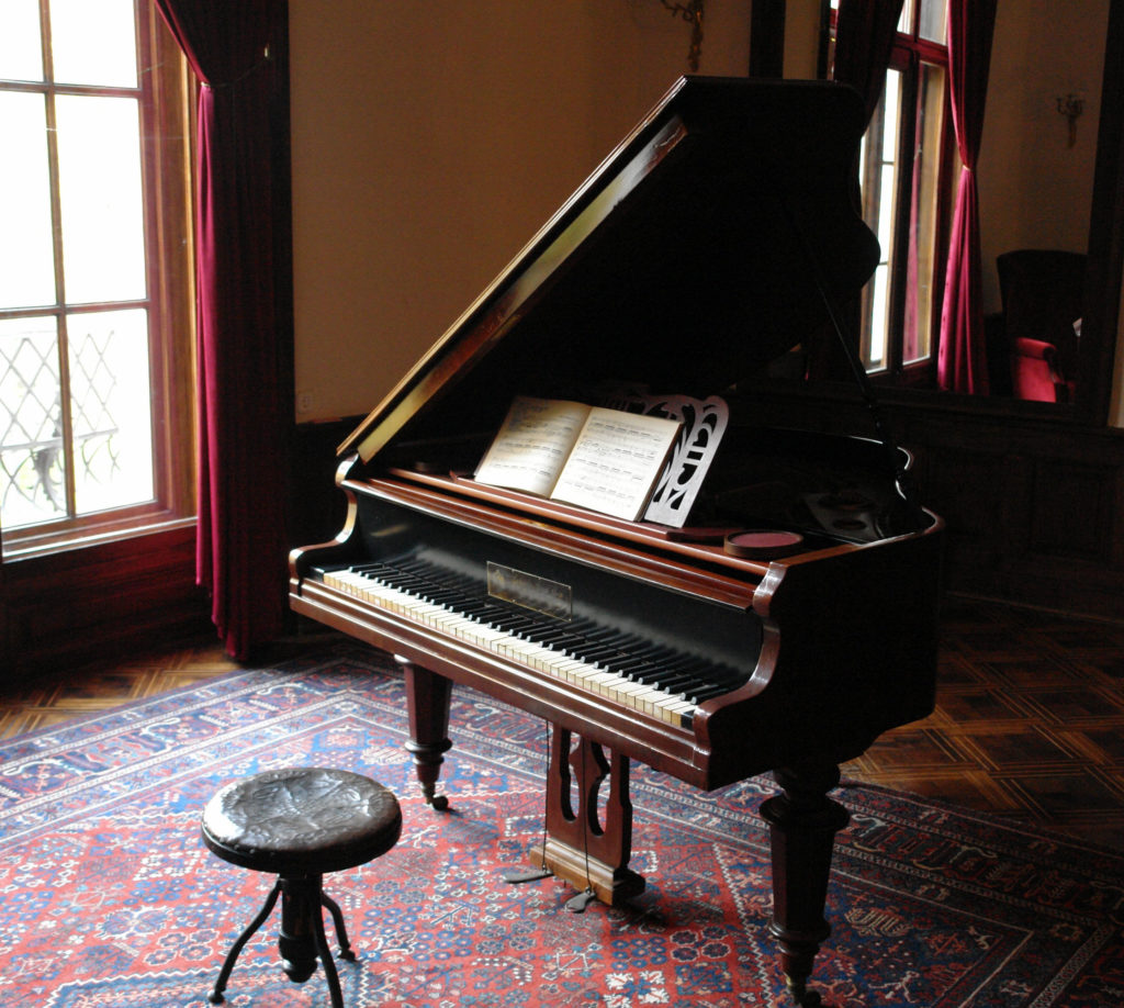 Vintage piano with sheet music and a stool inside a house near a window